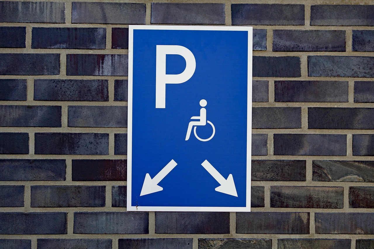 Blaues Schild mit Rollstuhlsymbol über einem markierten Behindertenstellplatz