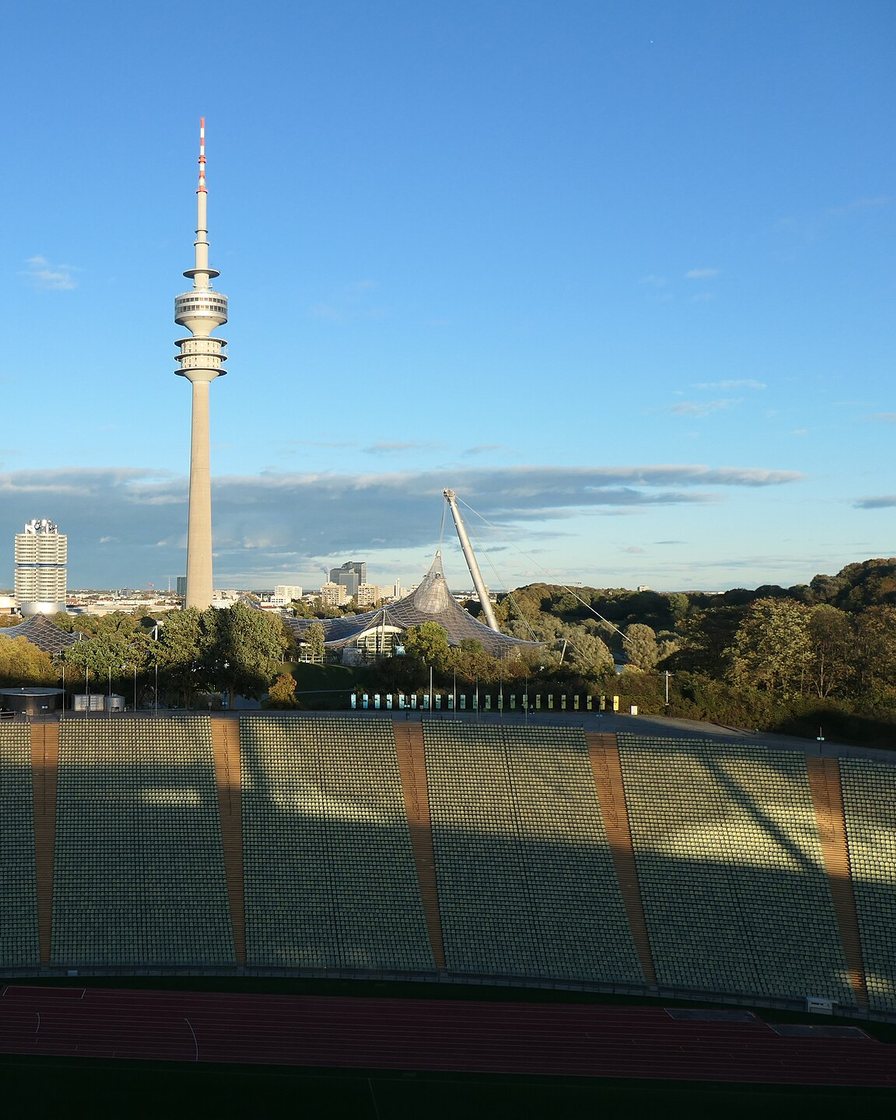 Blick über den See im Olympiapark München mit dem geschwungenen Zeltdach des Olympiastadions im Hintergrund