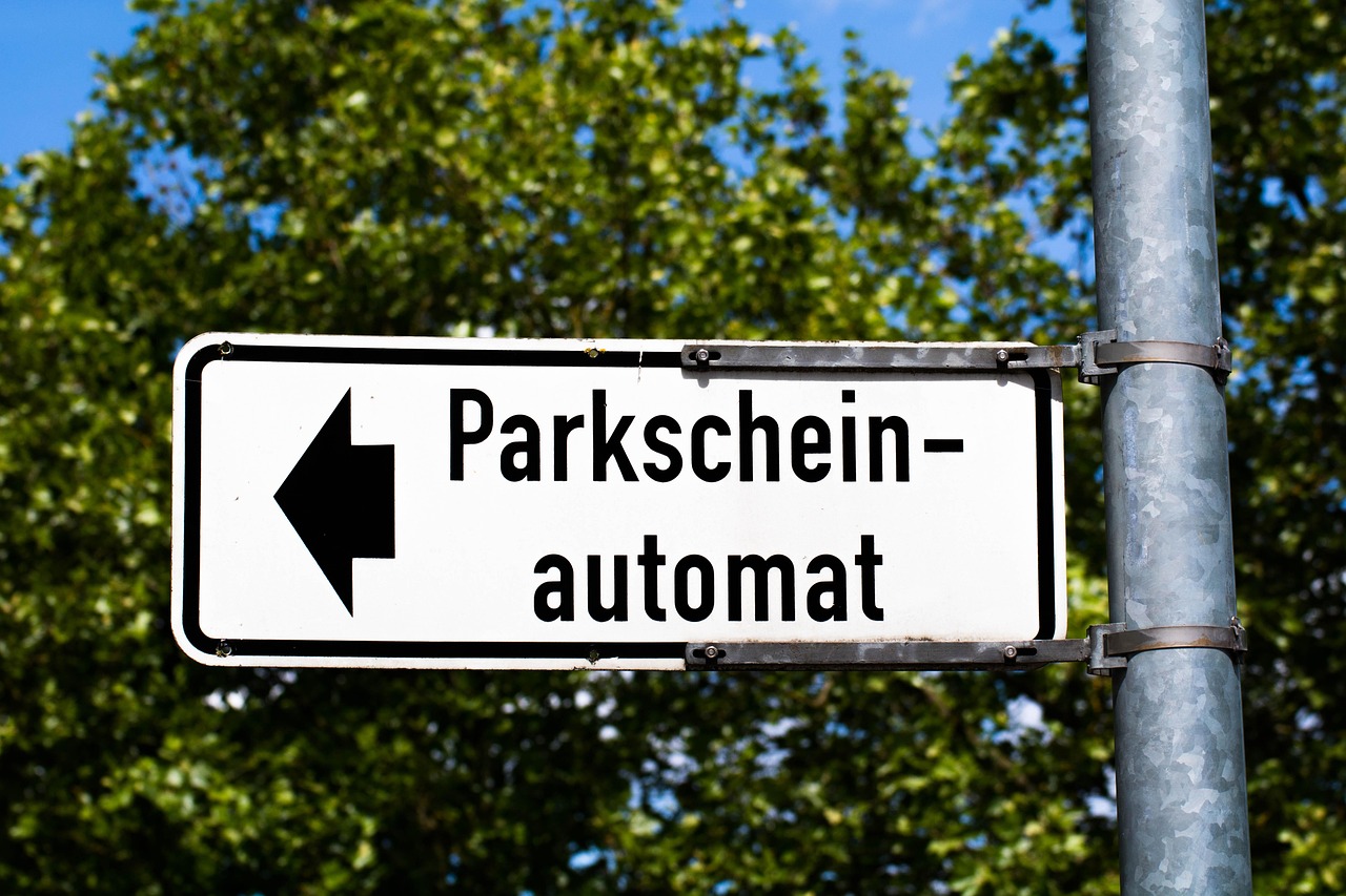 Parkscheinautomat am Straßenrand vor parkenden Autos und Zweirädern