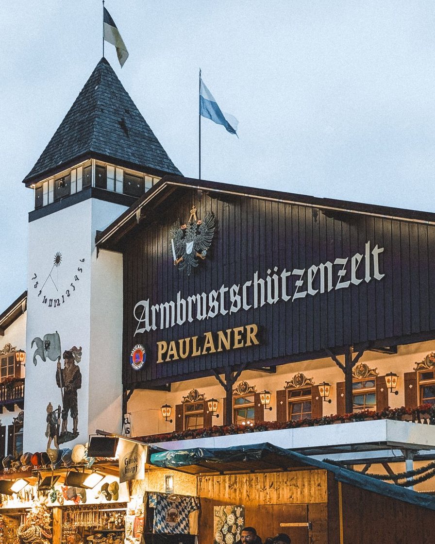Wartende Besucher in Tracht vor dem geschlossenen Seiteneingang eines großen Oktoberfest-Zeltes, Ordner in gelber Weste an der Tür